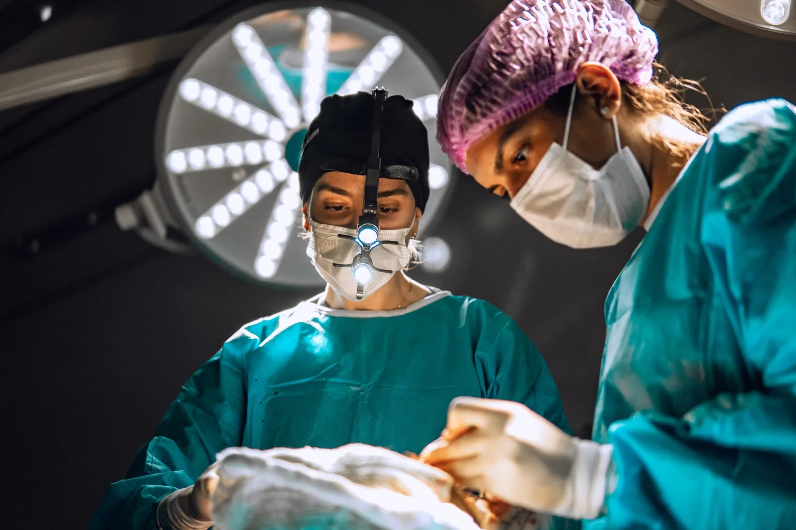 Dra. Rafaela Marques durante uma cirurgia, com a lupa e a luz de cabeça, ao lado da auxiliar