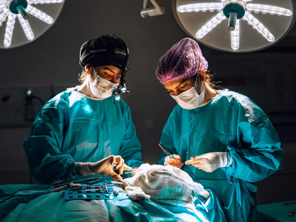 Dra. Rafaela Marques e a auxiliar durante uma cirurgia, sob o foco do centro cirúrgico