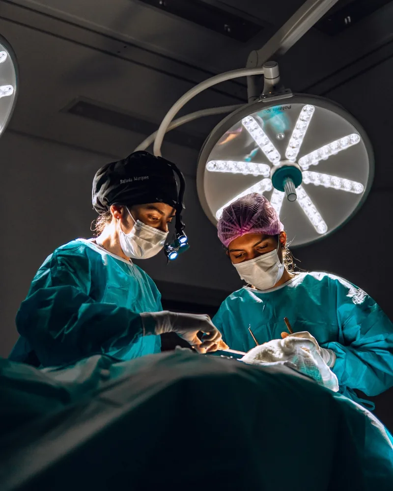 Dra. Rafaela Marques e a auxiliar durante uma cirurgia, sob o foco do centro cirúrgico