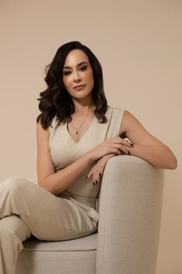 Dra. Rafaela Marques, cirurgiã plástica, em retrato sentada em uma poltrona clara